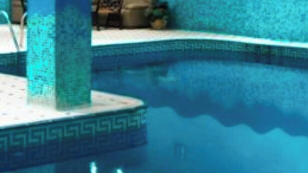 Una piscina con borde de azulejos, un área de descanso con un sofá y una pared decorativa.