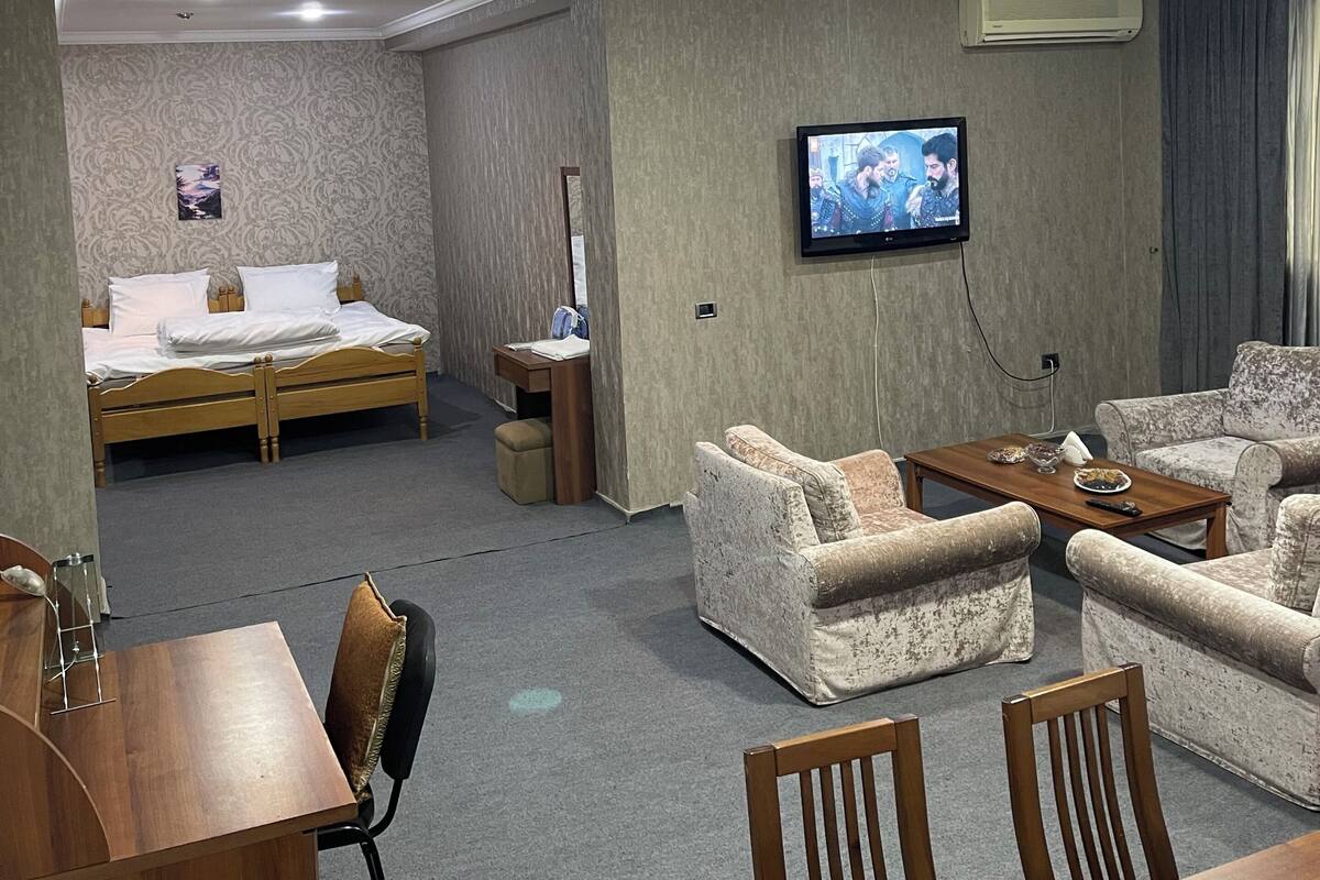 Hotellihuone, jossa on sänky, televisio, sohva, sohvapöytä ja työpöytä.