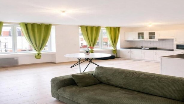 Een moderne woonkamer met een groene bank, een ronde tafel en een keuken op de achtergrond.