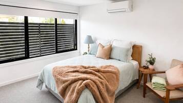 A bedroom with a large window, a bed with a blanket, a bedside table with a lamp, and a small plant.