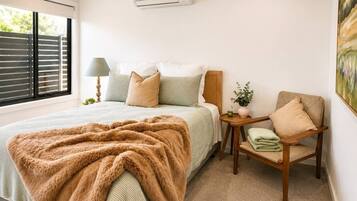 A bedroom with a bed, a chair, a nightstand, an air conditioner, and a window.
