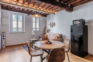 Una cucina moderna con frigorifero nero, tavolo da pranzo in legno e sedie, un divano e un soffitto con travi a vista.