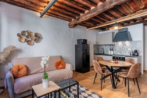 Una cucina moderna con un frigorifero nero, un tavolo da pranzo con sedie, un divano con cuscini decorativi e un lampadario.