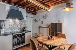 A kitchen with a stove, oven, and modern cabinetry, a dining table with chairs, and a rustic ceiling. - Appartamento Petri7 - Affitti Brevi Italia (Lucca)