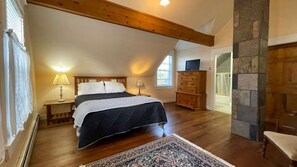 Une chambre à coucher comprenant un lit, des tables de chevet, une commode, un téléviseur et un mur en pierre.