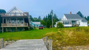 A two-story house with a balcony, a dock, and a car parked in the yard. - Seaside Friendship House on Lobster Cove (Jonesport)