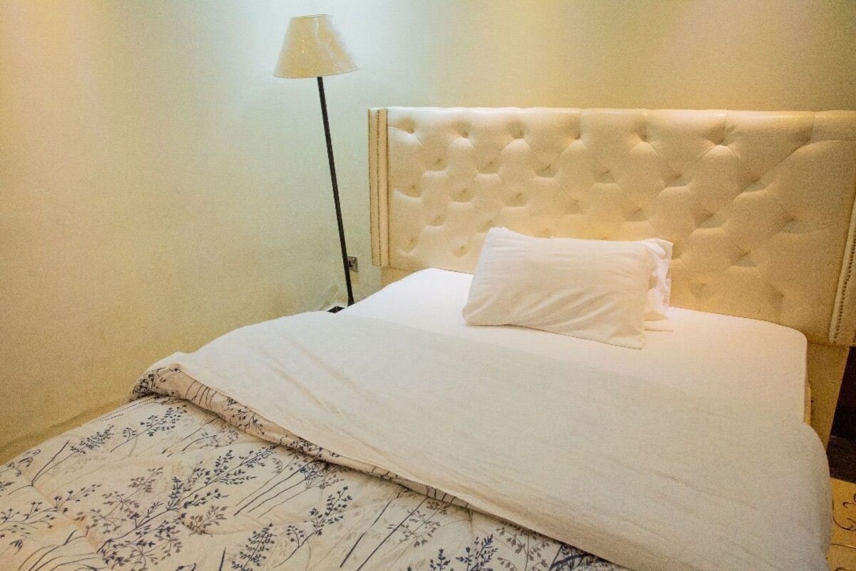A bed with a tufted headboard, a white pillow, and a floral-patterned bedspread.