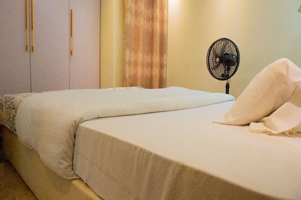 A bedroom with a bed, a fan, and a curtain. - Trucker's Rest House (Kigali)