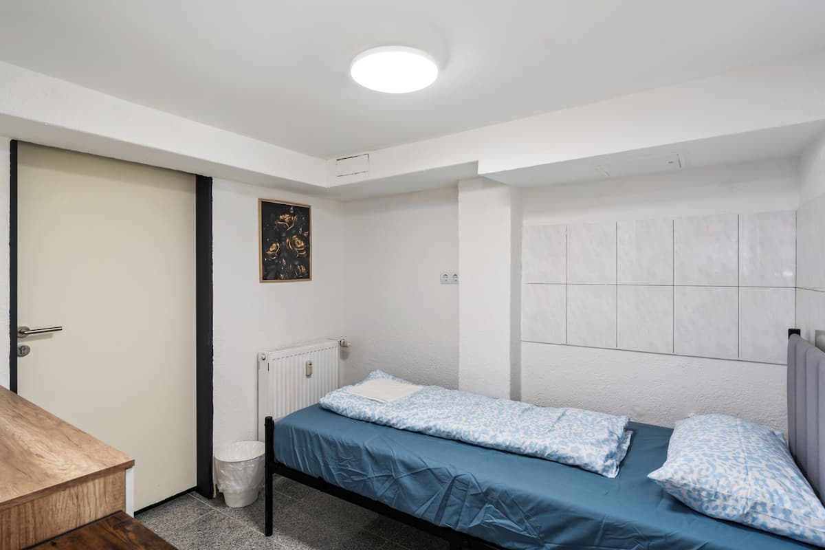 Un dormitorio con una cama individual, un escritorio de madera, un radiador y una pared blanca con un cuadro enmarcado.