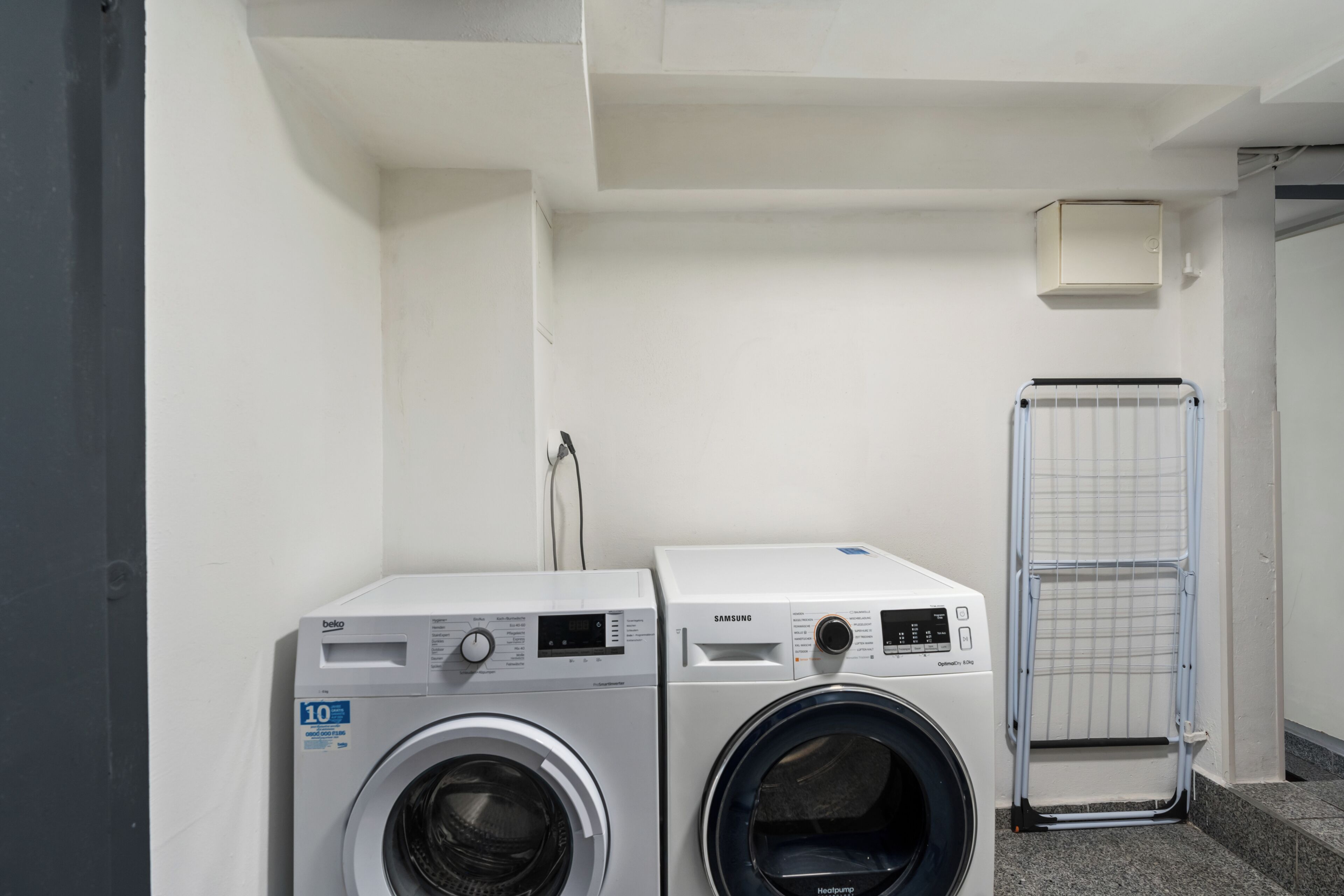 Un espace buanderie équipé de deux machines à laver, d’un étendoir et d’un radiateur fixé au mur.