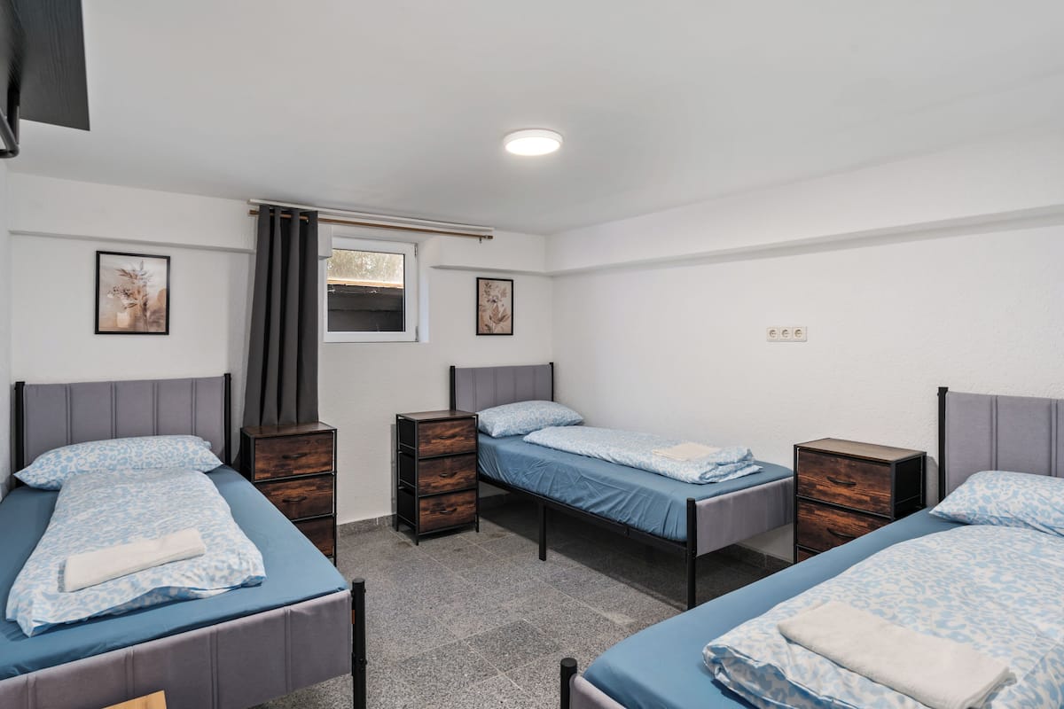 Una habitación con tres camas individuales, una ventana con cortinas, una lámpara de pared y un pequeño aparador.