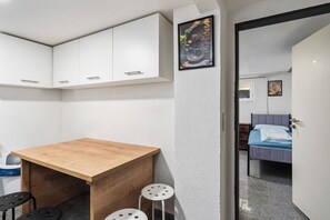 Una camera compatta con una scrivania in legno, due sgabelli, un letto e un quadro appeso alla parete.