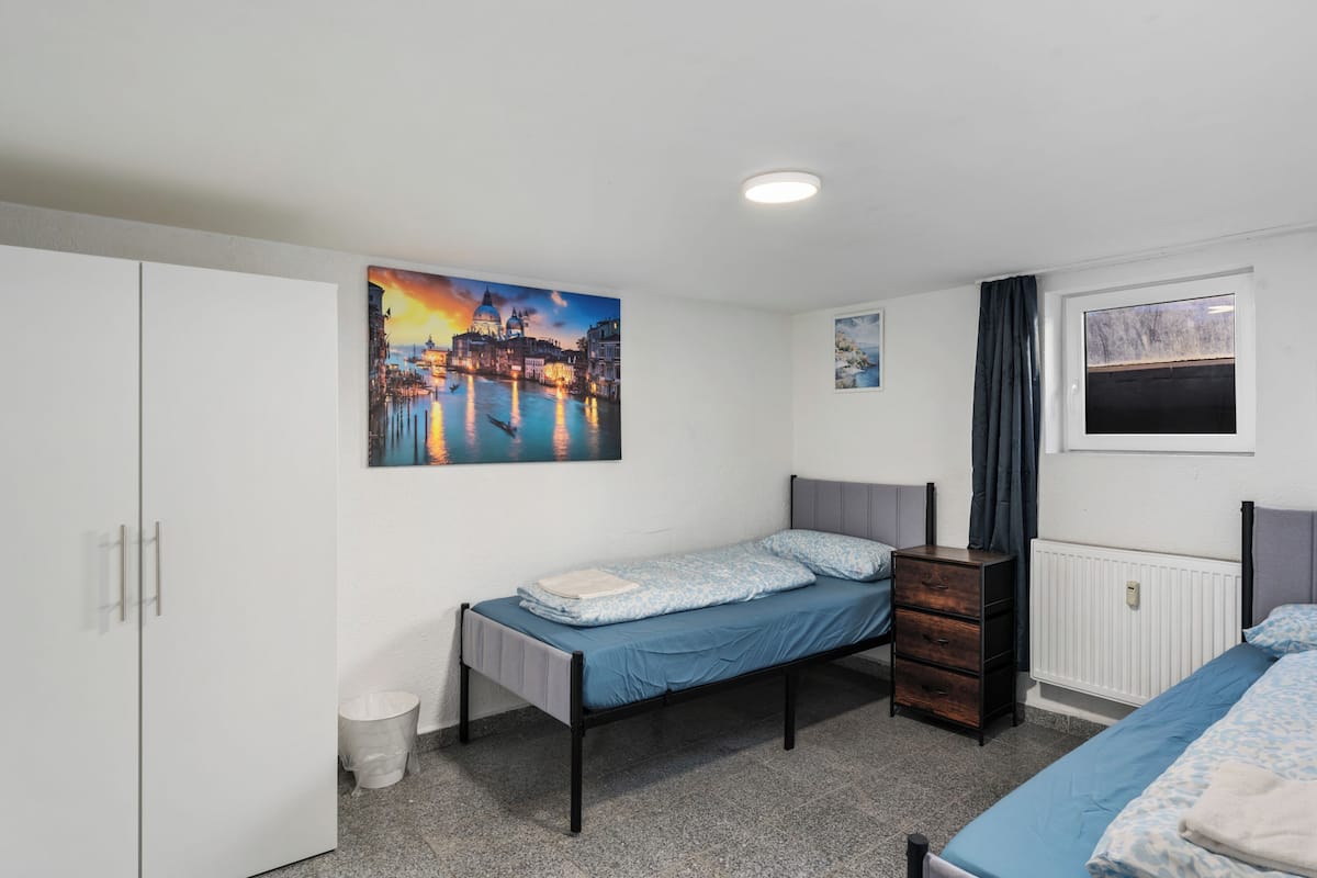 Un dormitorio con cama, cómoda, radiador y un cuadro de un paisaje urbano.