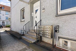Entrada de um edifício com porta branca, escada e caixa de correio.