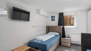 Un dormitorio con cama, televisor, una mesita, ventana con cortinas y radiador.