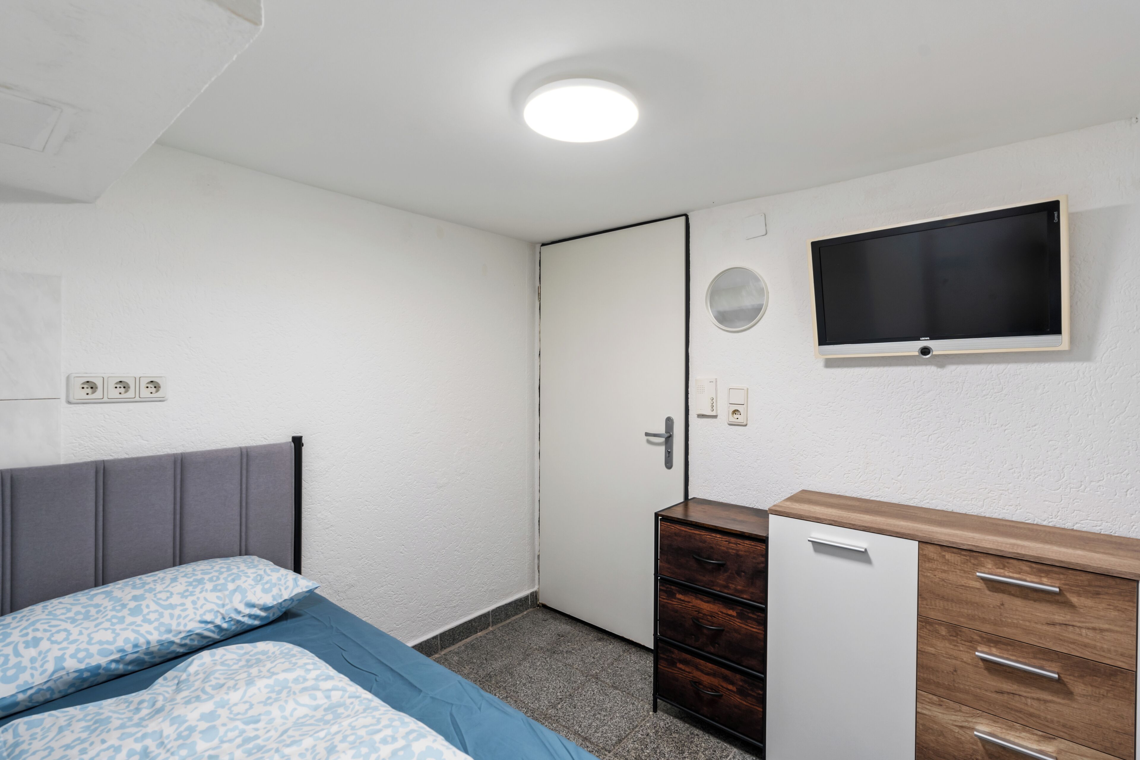 Ein Schlafzimmer mit einem Bett, einem Schminktisch, einem Fernseher und einer Tür.