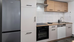 A modern kitchen with a stainless steel refrigerator, a built-in oven, a dishwasher, and wooden cabinets.