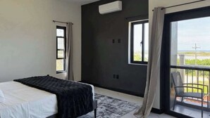 Een moderne slaapkamer met een bed, een raam, een airconditioning en een balkon met een stoel.