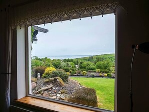 A window with a view of a landscaped garden, a stone structure, and a body of water. - House of the Sea - Camp (Kilgobban)