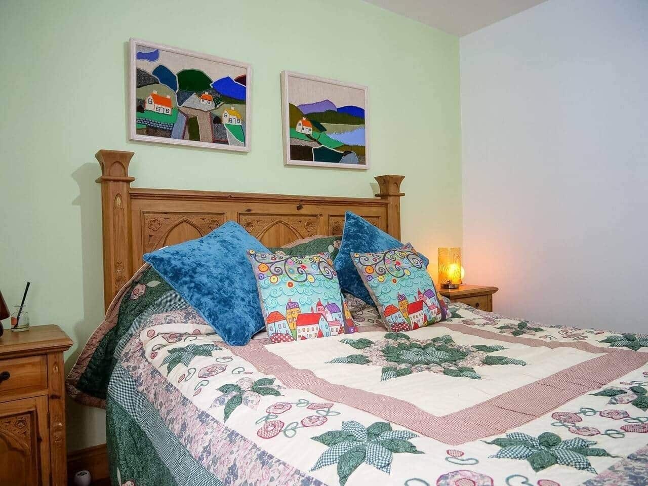 A bed with a floral quilt, two wall-mounted paintings, and a bedside lamp.