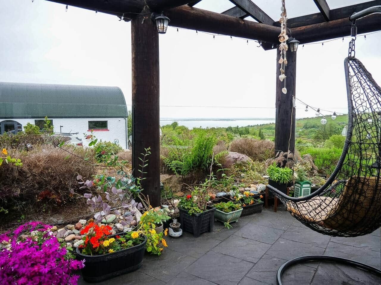 Une terrasse de jardin avec un fauteuil suspendu, des plantes en pot et une vue sur la mer.