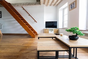 Een kamer met een houten trap, een televisie, een houten tafel en een bonsaitje.