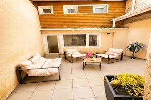 Une petite terrasse avec un canapé, deux chaises, une table et une plante en pot.