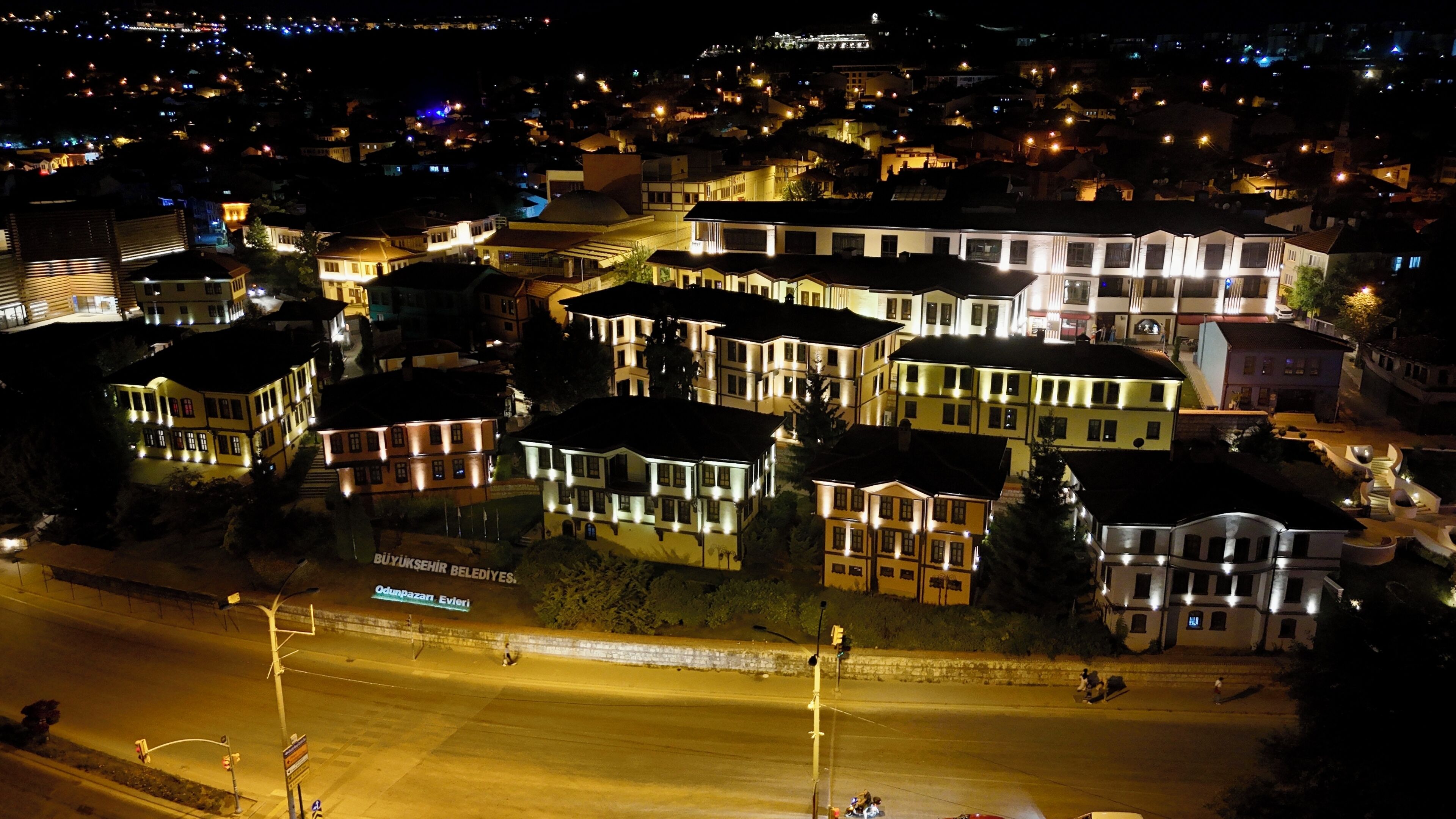 A nighttime aerial view of a residential area with multiple buildings, a clear road, and streetlights.