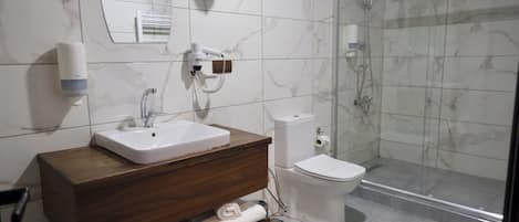 A bathroom with a marble-tiled wall, a white sink, a toilet, a glass-enclosed shower, and a wooden vanity with towels.