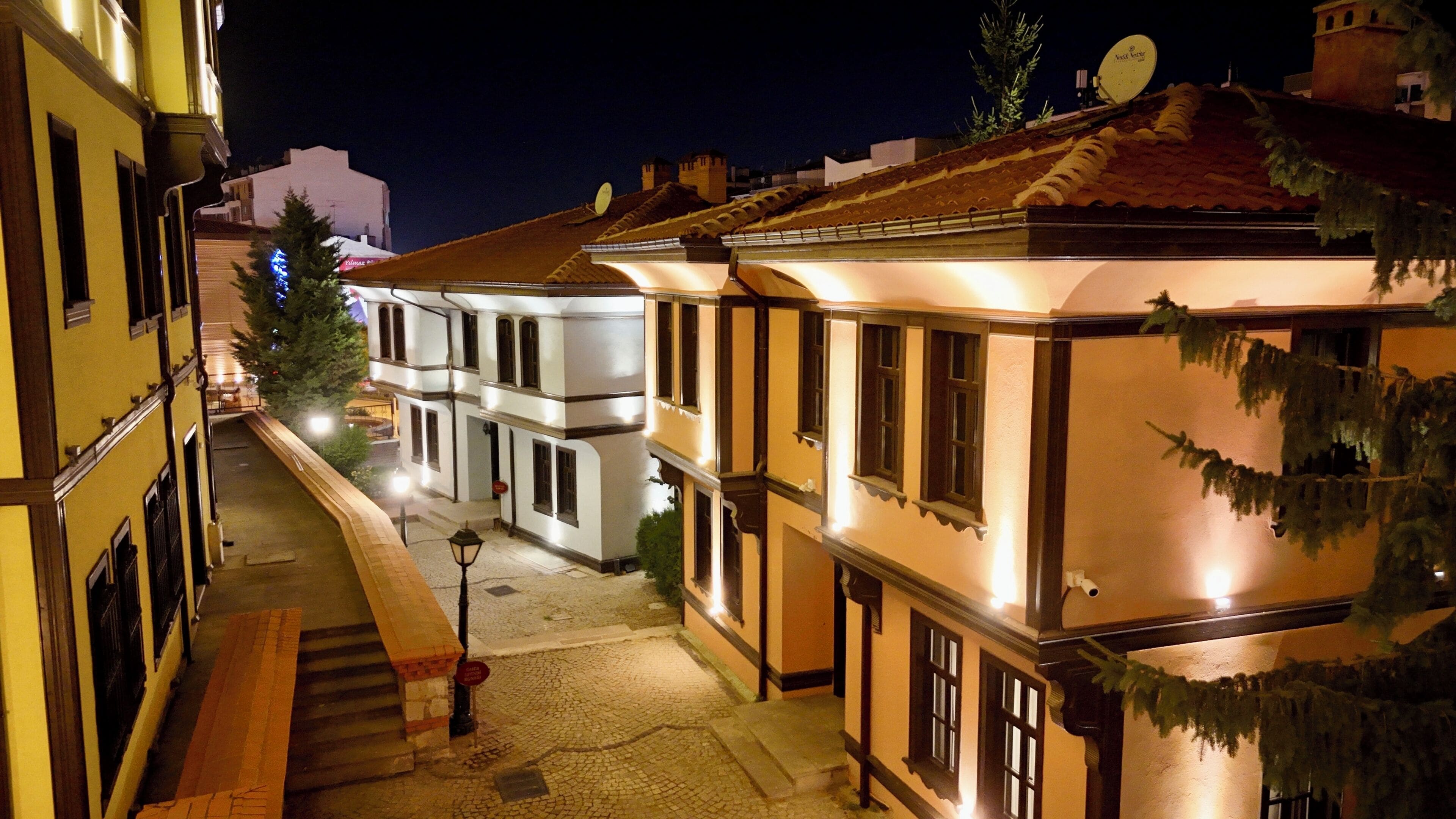 Vista nocturna de una calle estrecha flanqueada por edificios, con un camino adoquinado y un farol.