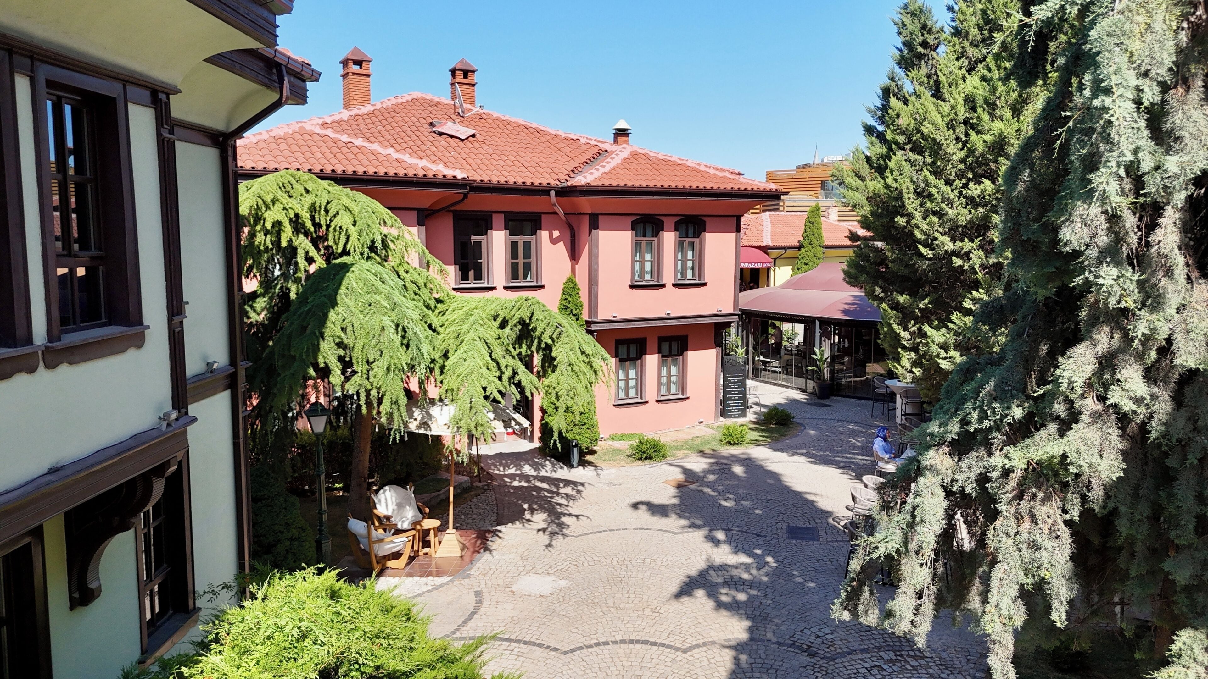 Ein Innenhof mit einem Gebäude, das ein Ziegeldach, eine überdachte Sitzgelegenheit und einen gepflasterten Weg aufweist.