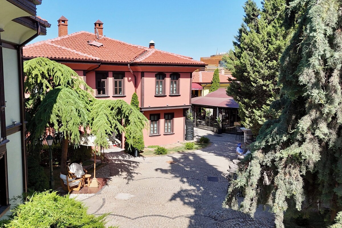 Un patio con un edificio que tiene techo de tejas rojas, un área de estar al aire libre techada y un sendero de adoquines.