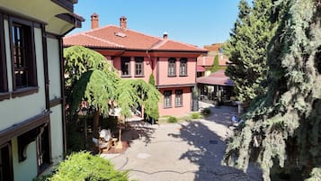 A courtyard with a building featuring a red-tiled roof, a covered outdoor seating area, and a cobblestone path.