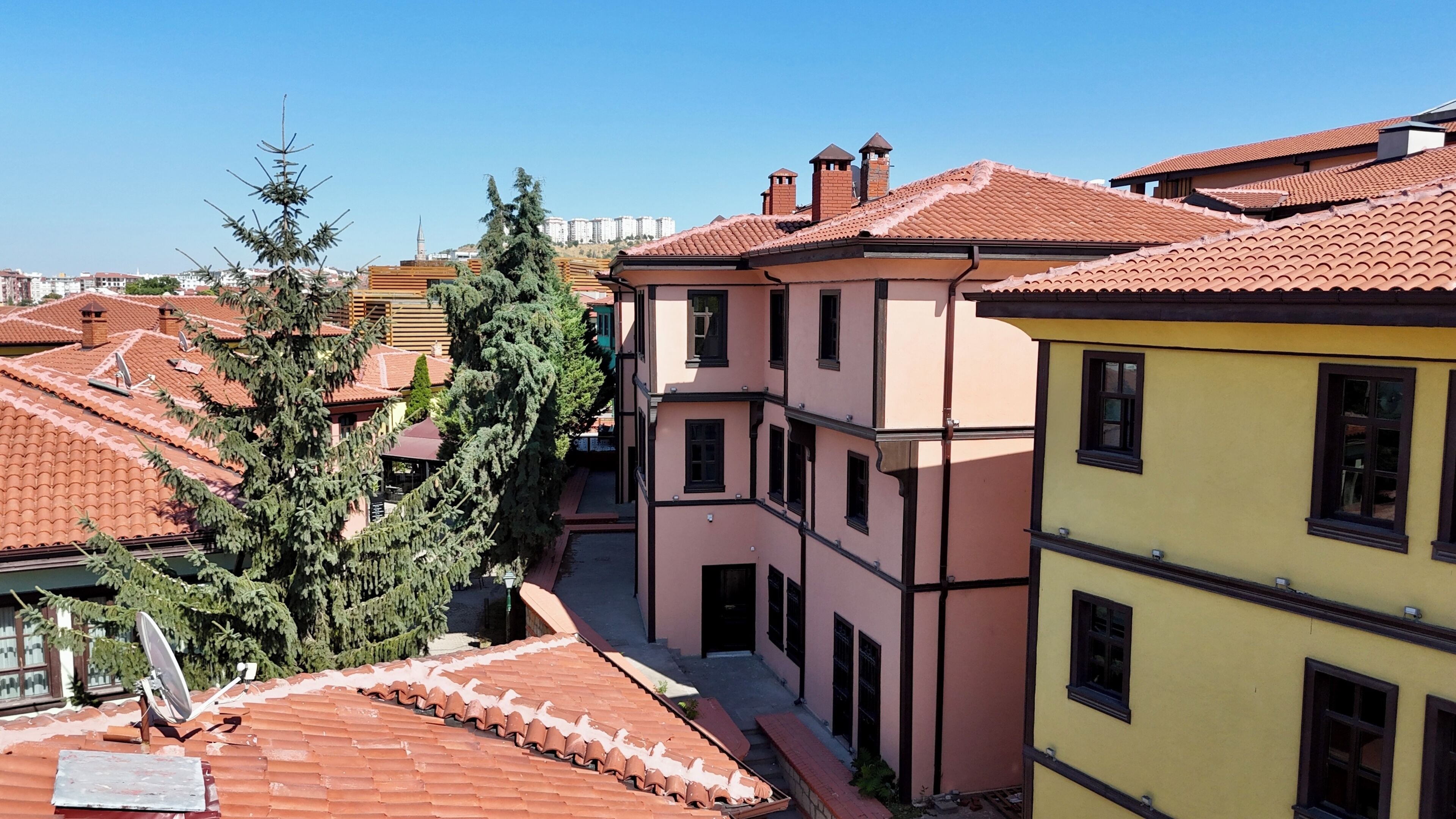 A multi-story building with a red-tiled roof, a satellite dish, and a clear sky.