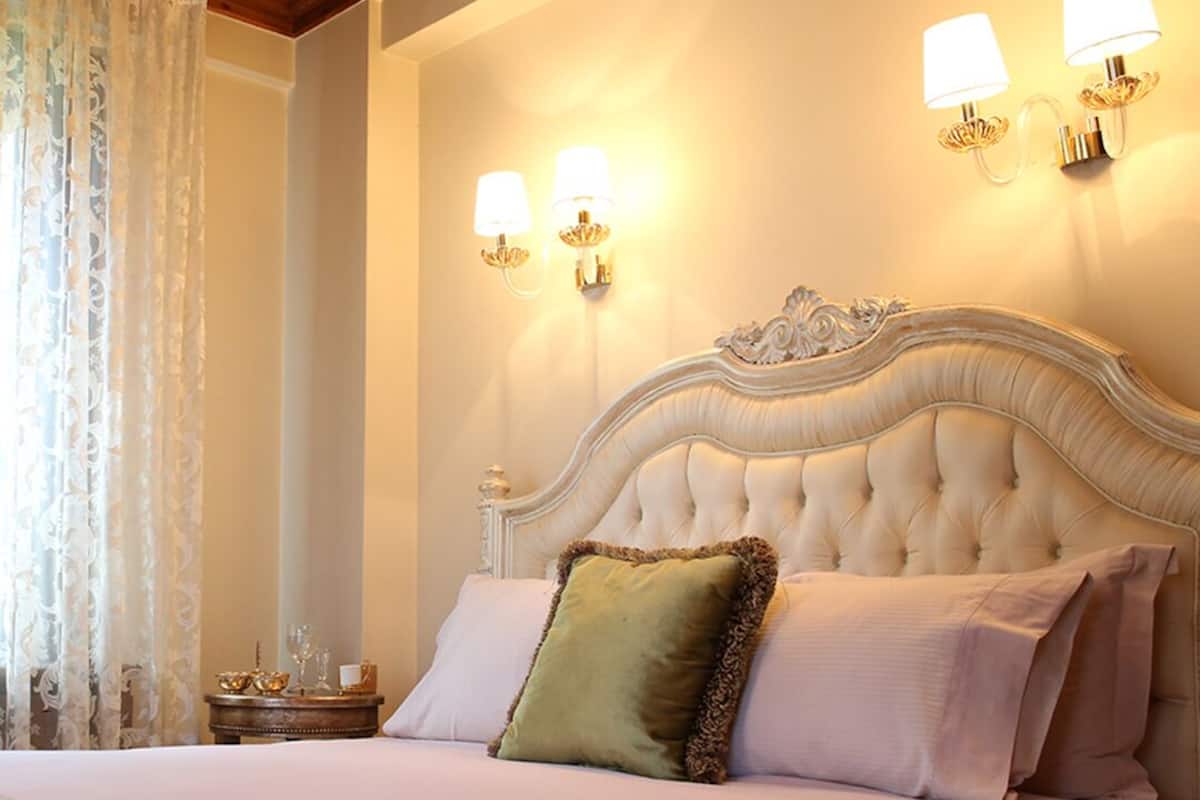A bedroom with a tufted headboard, two wall-mounted lamps, a bedside table with a lamp, and a decorative item.