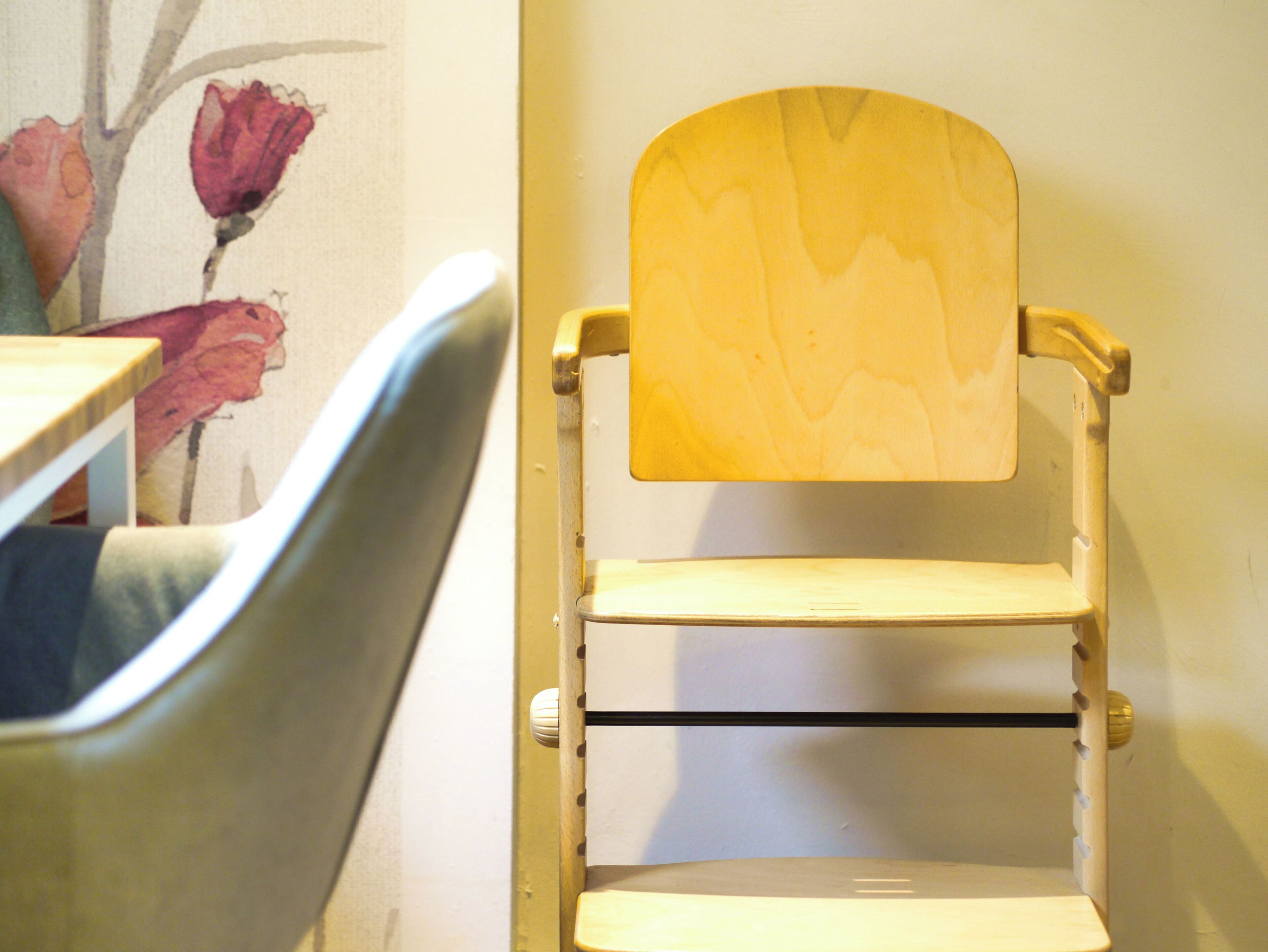 A chair with a wooden backrest and a metal frame, positioned next to a wall with a floral painting.