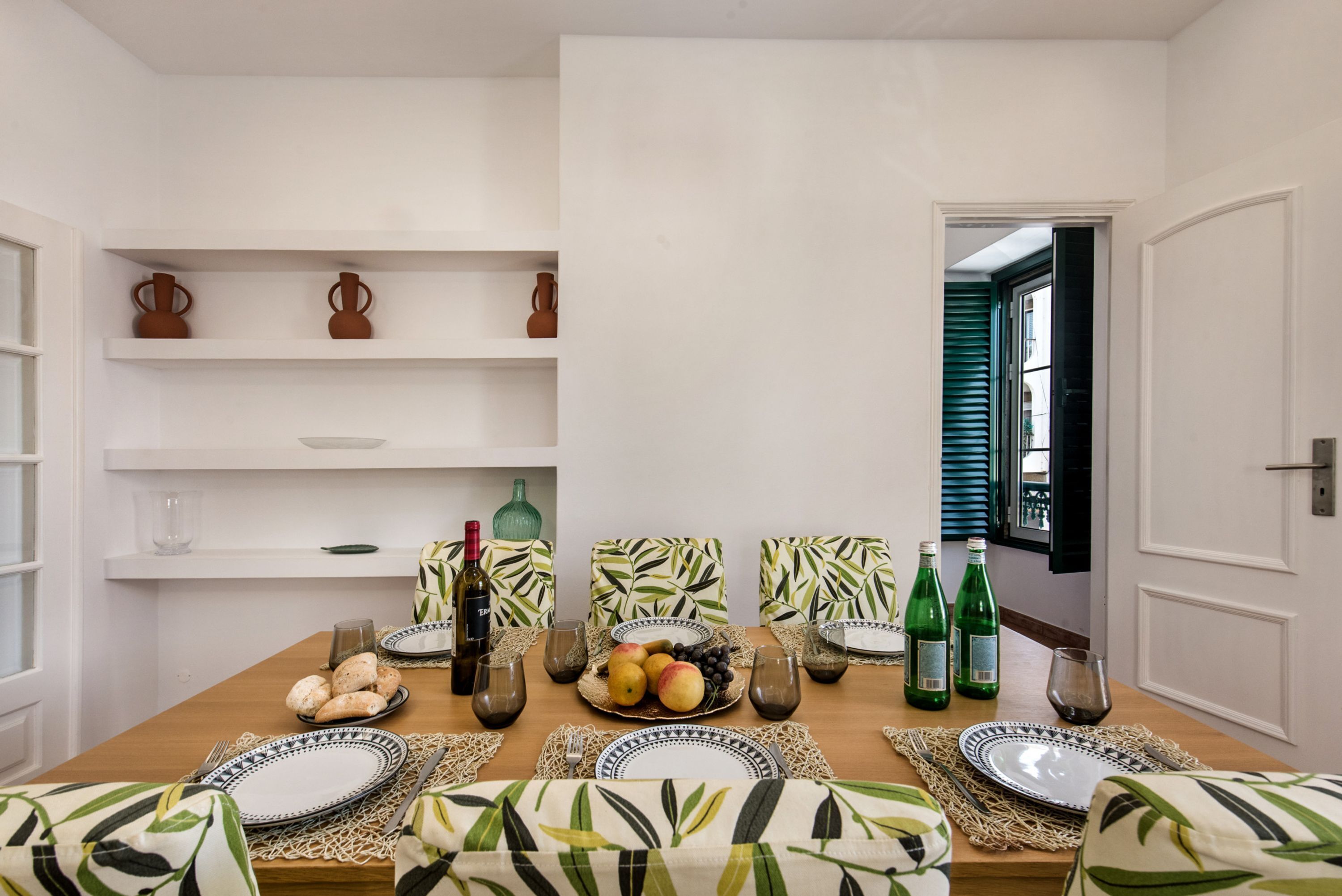 Uma área de refeições com uma mesa de madeira posta para quatro pessoas, rodeada por almofadas estampadas.