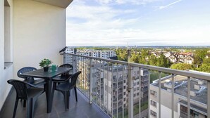 En balkong med ett bord och stolar, en krukväxt och utsikt över staden.