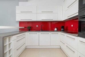 Een moderne keuken met witte kasten, een rode achterwand en een aanrecht van roestvrij staal.