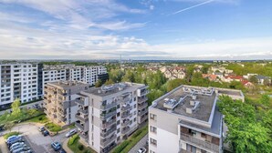 En hög byggnad med många våningar, avsedd för bostäder, med flera balkonger, en parkeringsplats och utsikt över en avlägsen stadsbild.