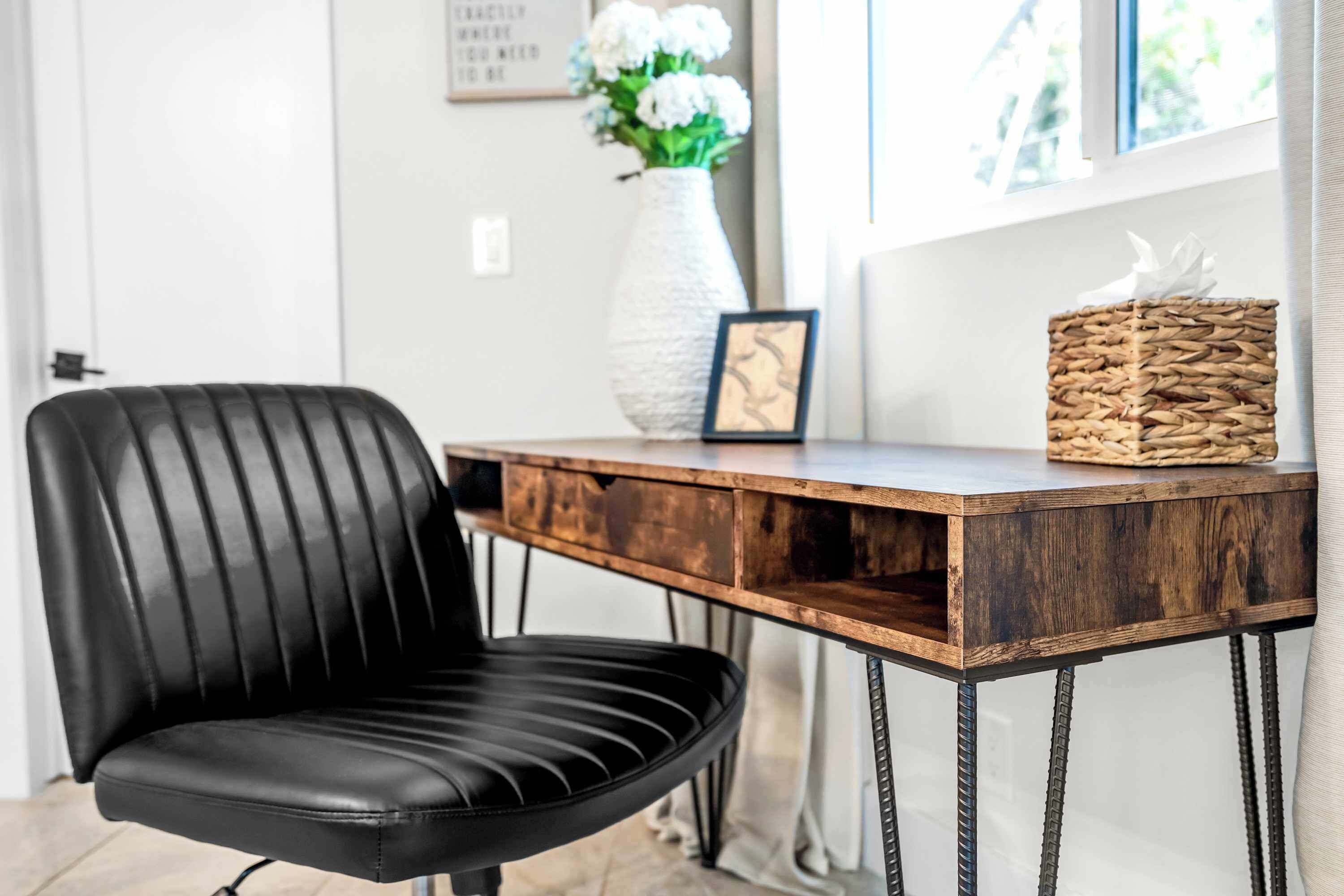 Una poltrona in pelle nera, un tavolo di legno con gambe metalliche, un vaso bianco con fiori e un quadro incorniciato sul tavolo.