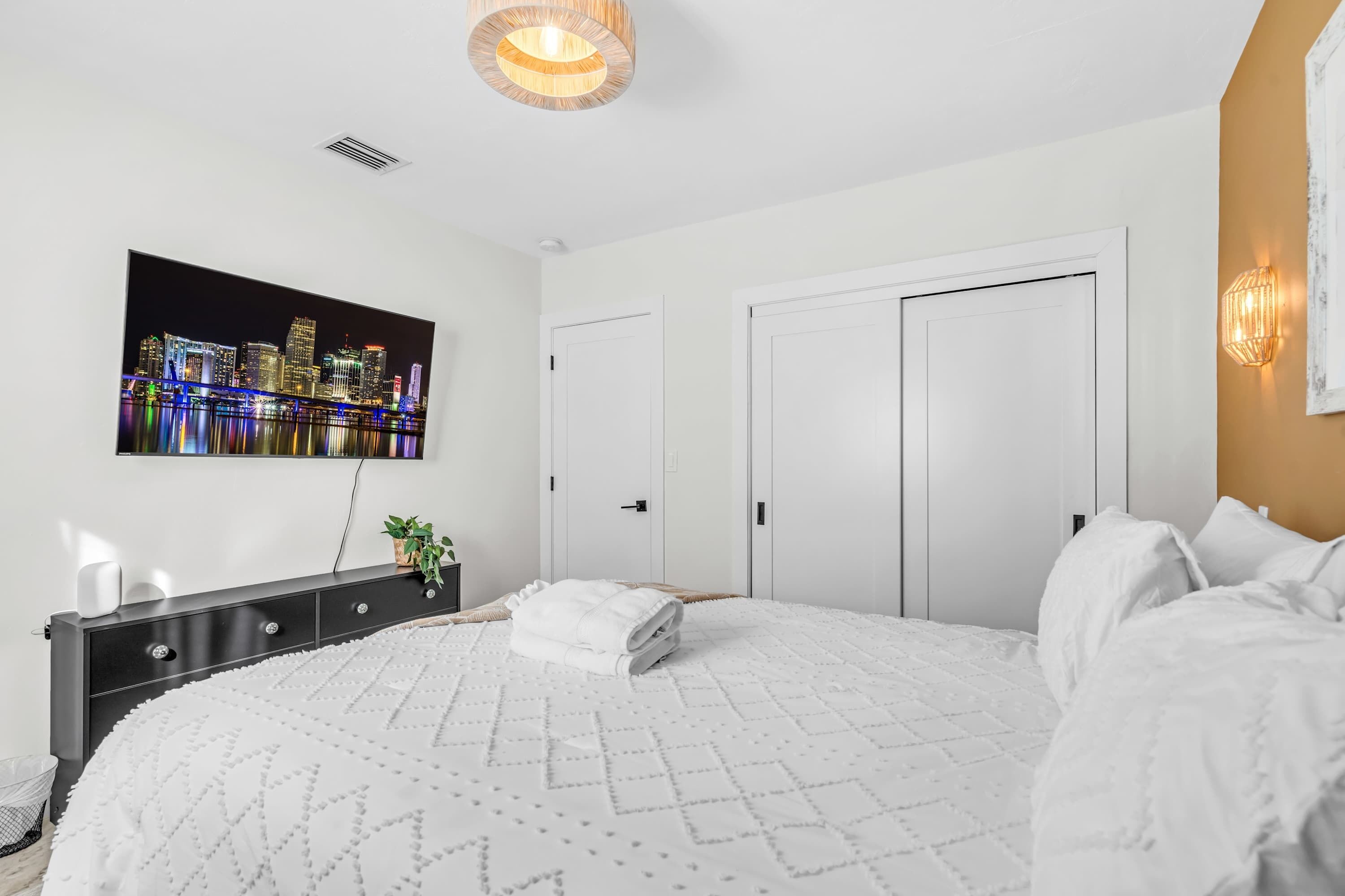 Ein Schlafzimmer mit Bett, Kommode, Wand-Fernseher und einer Tür.