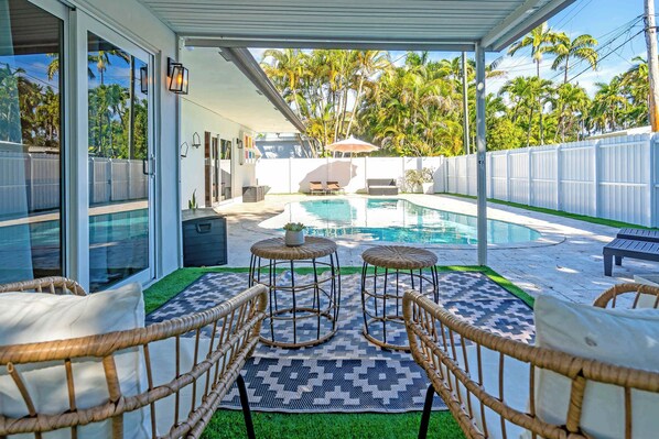 A covered outdoor area with a pool, wicker furniture, and a view of palm trees. - Sunny House With Pool - Spacious (Hollywood)