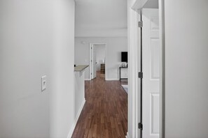 Un pasillo con paredes blancas y suelo de madera que conduce a una zona de cocina con un televisor montado en la pared.