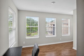 A room with three windows, a dining table, and a chair.