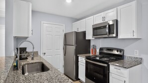 A kitchen with white cabinets, stainless steel appliances, granite countertops, and a double sink.