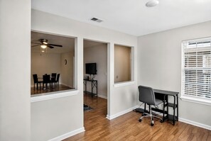 A room with a ceiling fan, a desk with a chair, a TV, and a window with blinds.