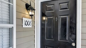 A black door with a keypad lock, a number sign '1008' above it, and a wall-mounted lantern to the left.
