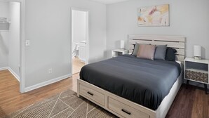 A modern bedroom with a large bed, bedside tables, a nightstand, and a painting on the wall.