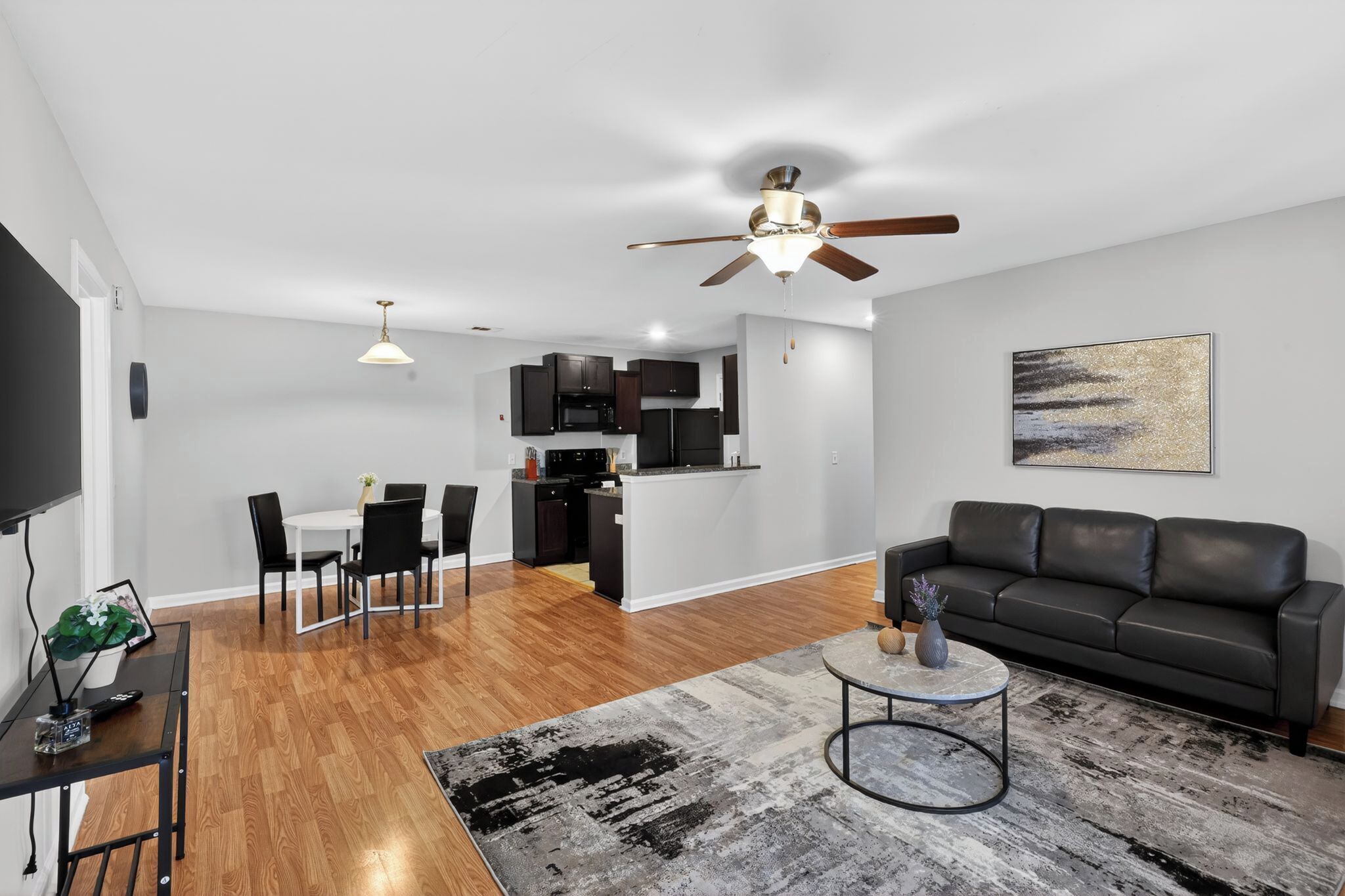 A modern living room with a black leather sofa, a round coffee table, and a dining area with a white table and black chairs.